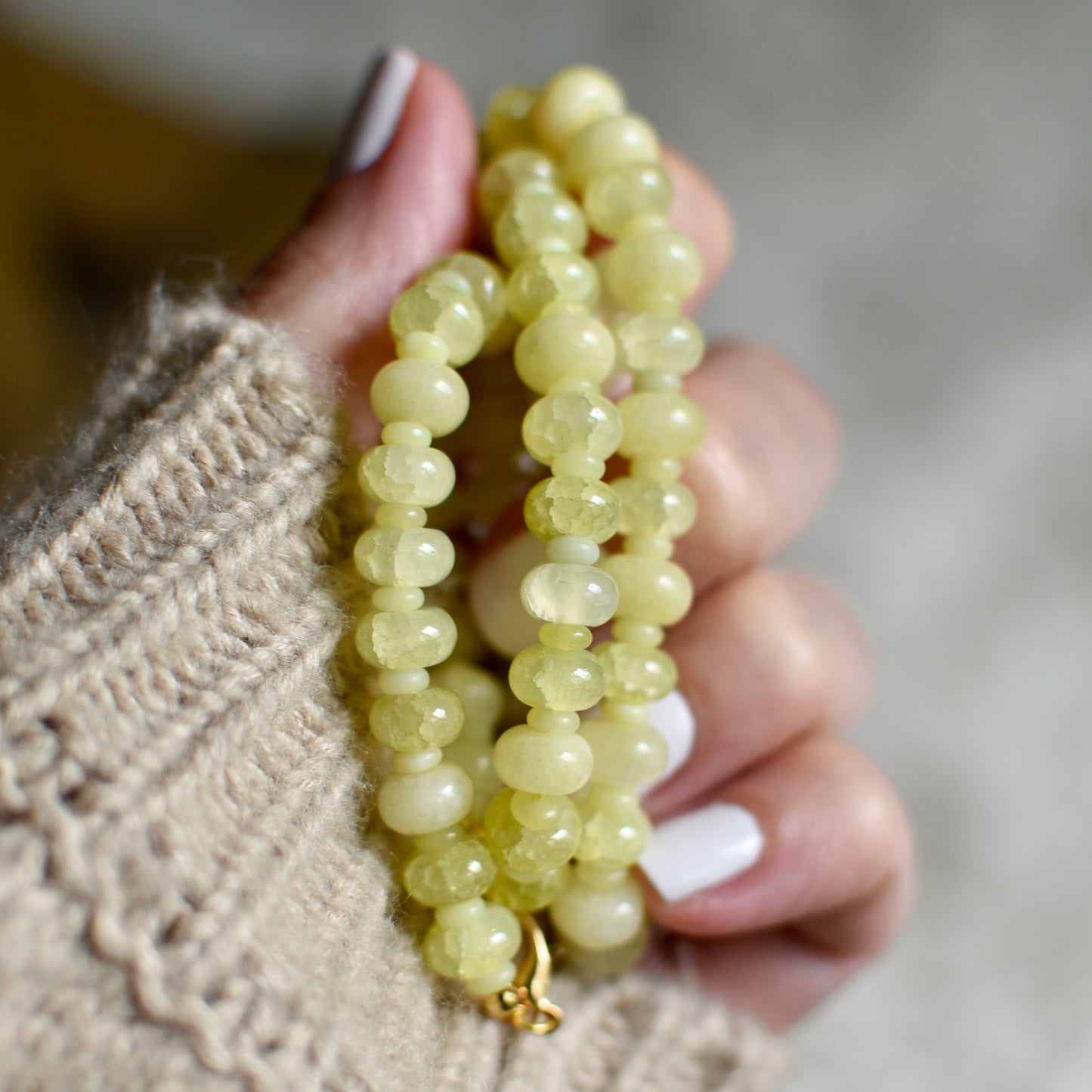 Hand holding a string of light yellow beads against a blurred background