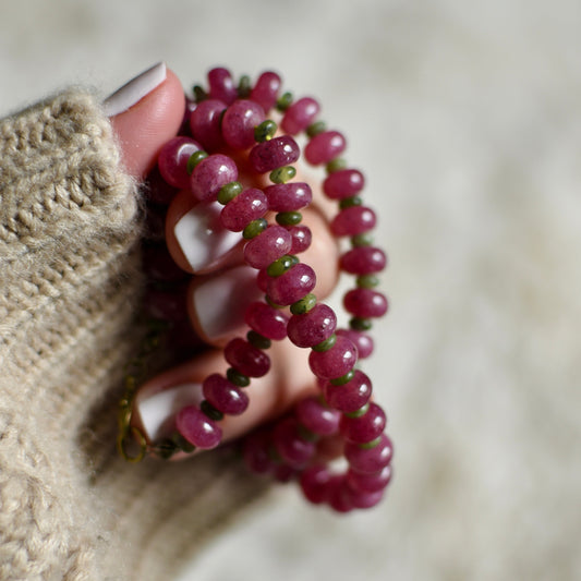 Hand holding a pink beaded necklace against a neutral background