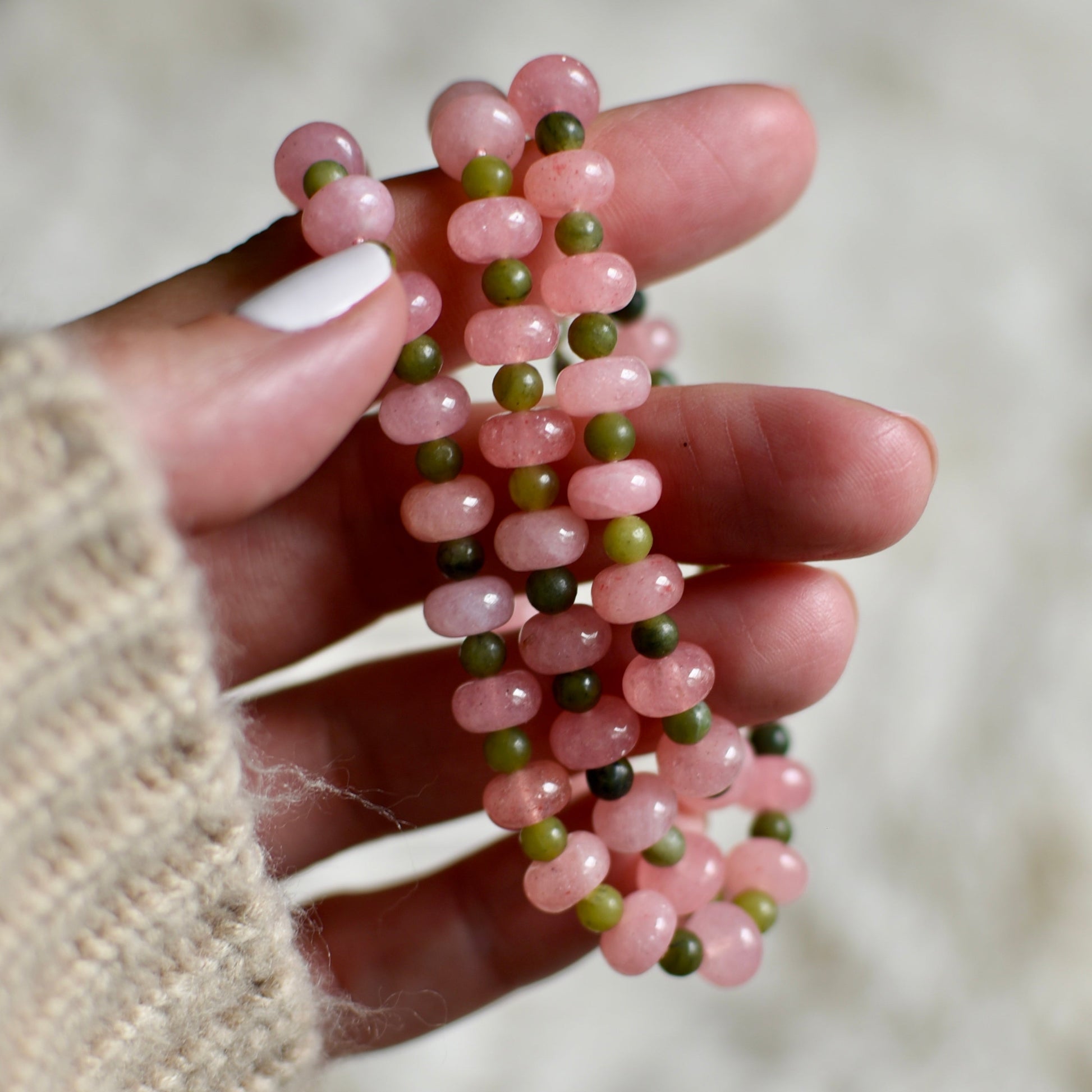 Hand holding a pink and green beaded necklace against a blurred background