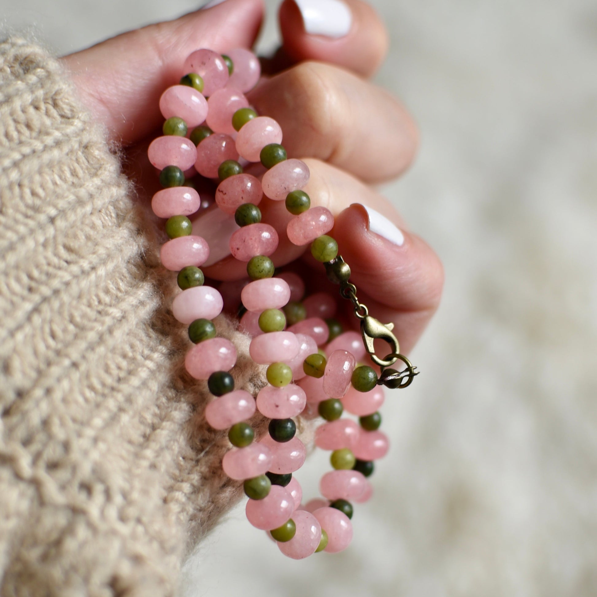 Hand holding a pink and green beaded necklace against a blurred background