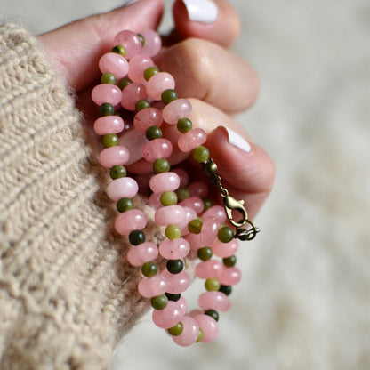 Hand holding a pink and green beaded necklace against a blurred background