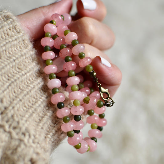 Hand holding a pink and green beaded necklace against a blurred background