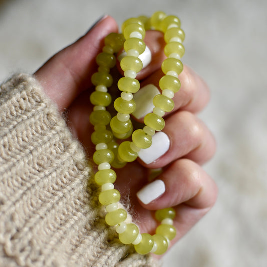 Hand holding a green beaded bracelet against a blurred background