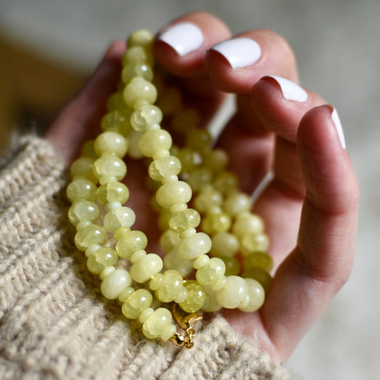 Hand holding a string of light yellow beads against a blurred background