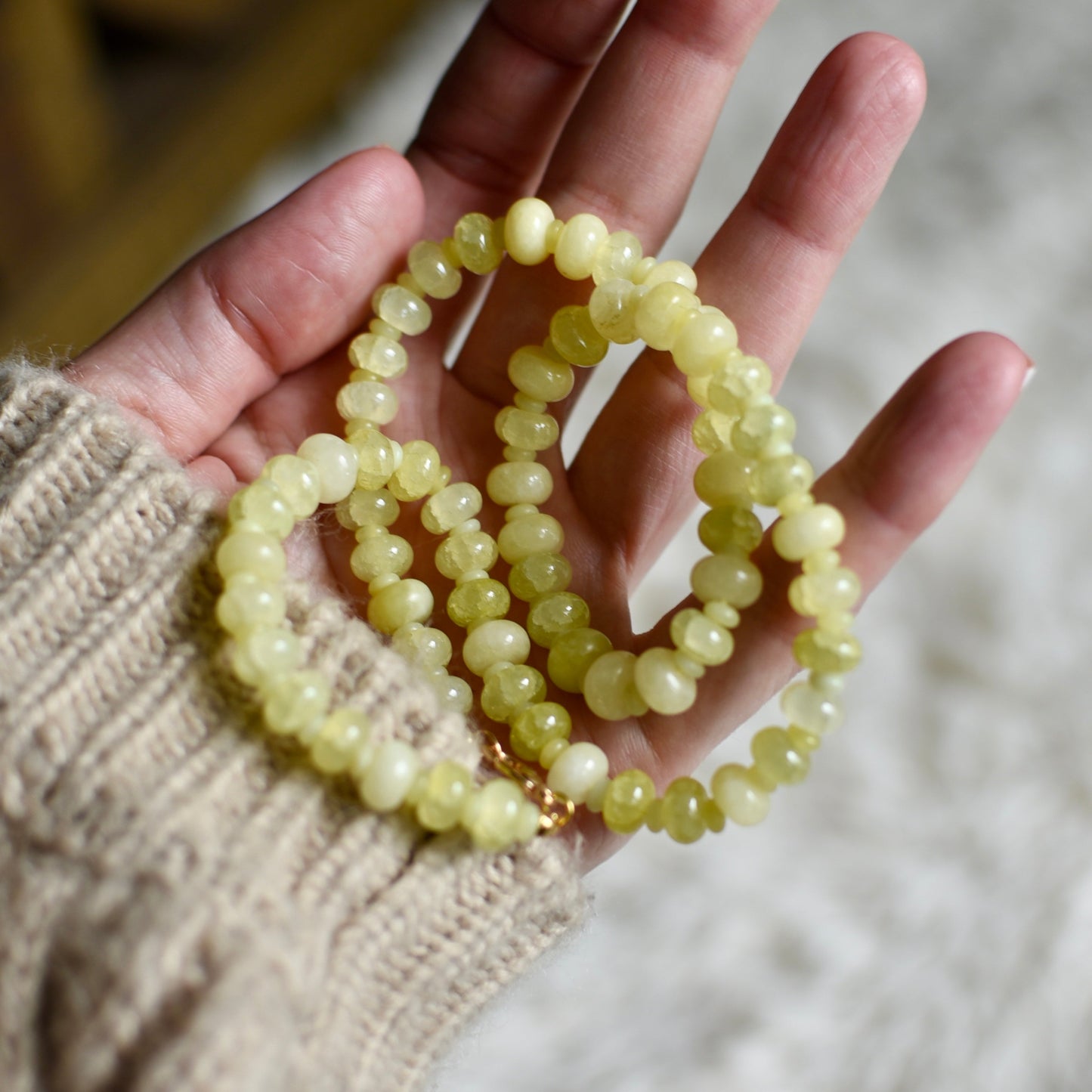 Hand holding a string of light yellow beads against a blurred background