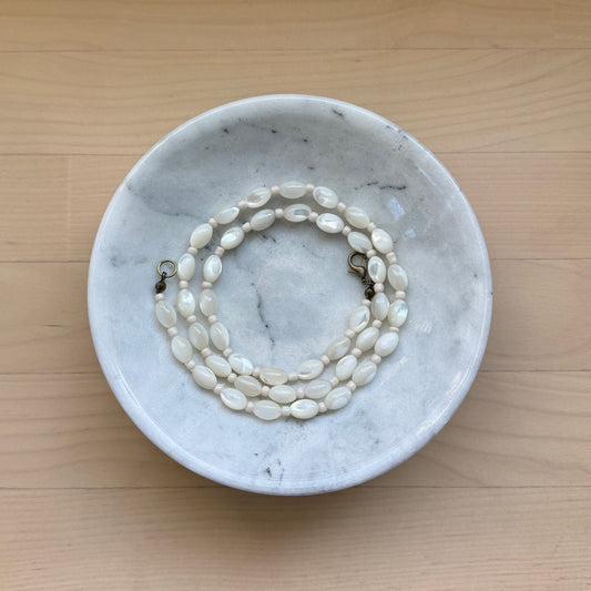 Marble dish with a pearl necklace on a wooden surface