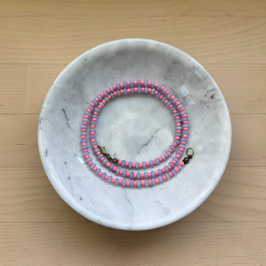 Pink and purple beaded necklace in a marble bowl on a wooden surface
