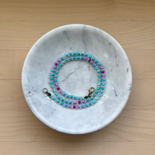 Marble jewelry dish with a beaded necklace on a wooden surface