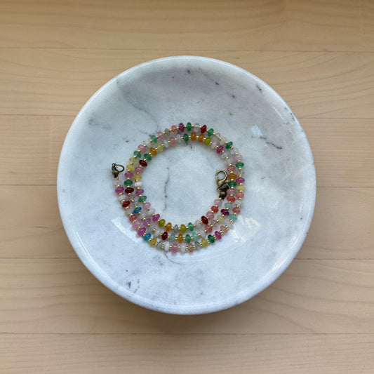 Colorful beaded bracelet in a white marble dish on a wooden surface