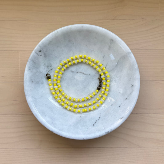 Marble-patterned dish with a yellow beaded bracelet on a wooden surface