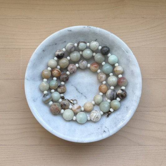 Beaded necklace in a marble dish on a wooden surface