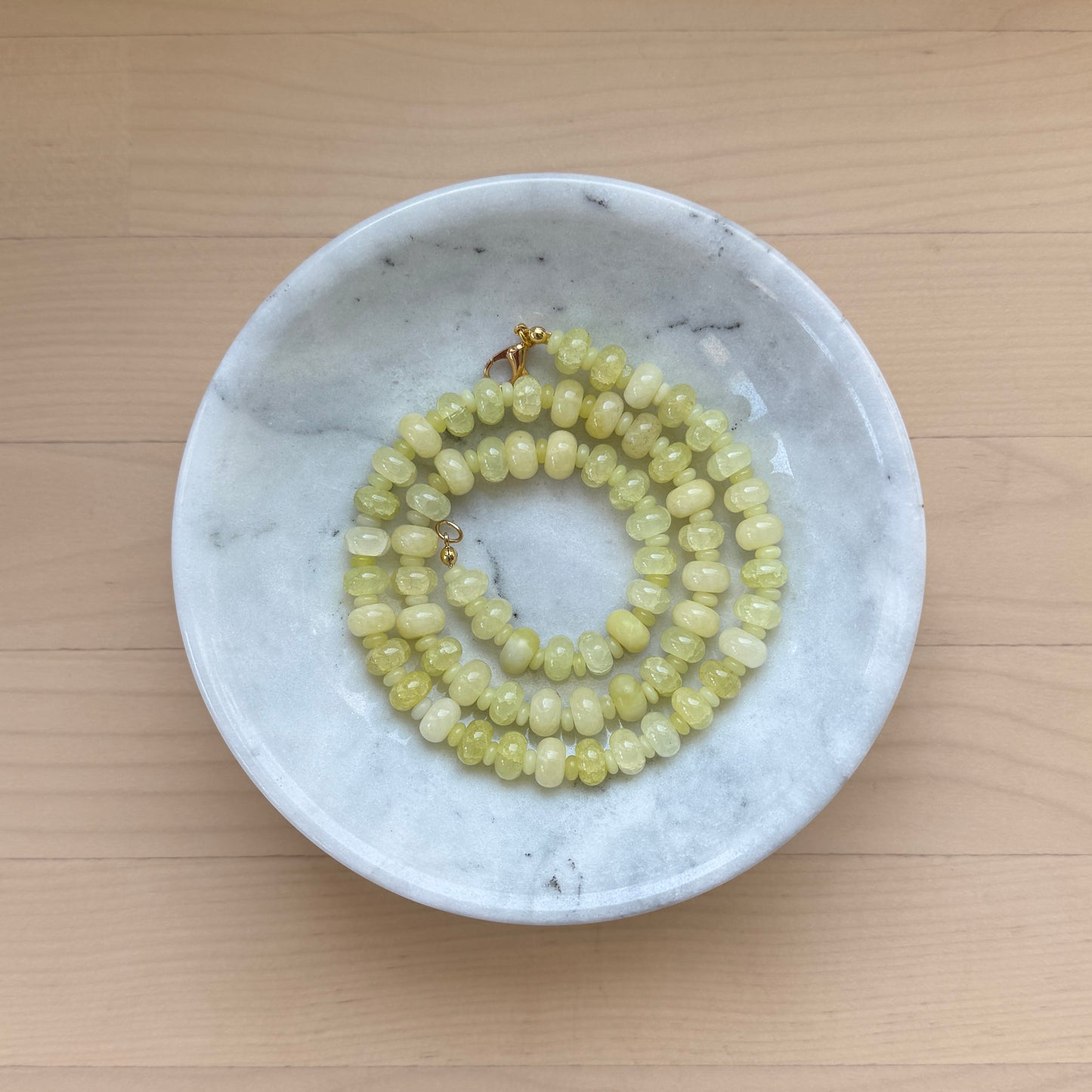 Necklace with green beads in a white marble dish on a wooden surface