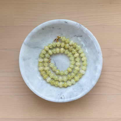 Necklace with green beads in a white marble dish on a wooden surface