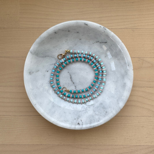 Marble-patterned dish with a beaded necklace on a wooden surface