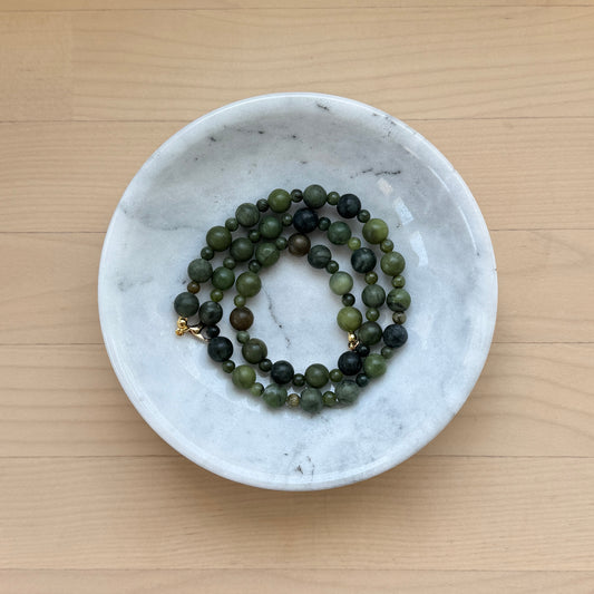 Green beaded necklace in a white marble dish on a wooden surface